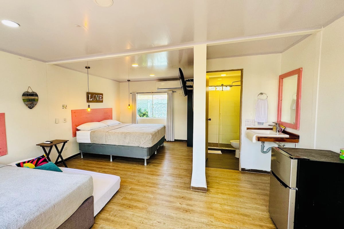 A hotel room with two beds, a wooden floor, a bathroom with a shower, and a sink.