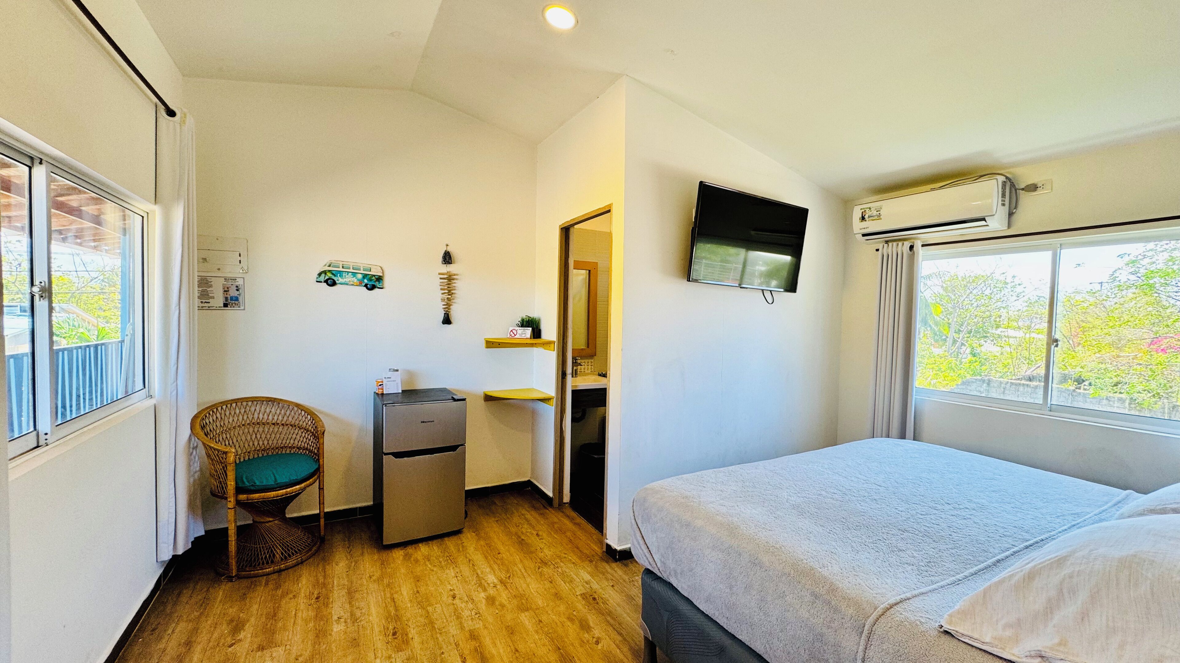 A compact room with a bed, a chair, a desk with a computer, a TV, and an air conditioner.