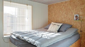 Une chambre à coucher avec un lit, une fenêtre avec des stores et un mur recouvert d’un panneau de bois.