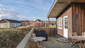 Un bâtiment en bois doté d’un balcon, aménagé avec des chaises et une table en osier, qui donne sur une zone herbeuse, avec d’autres bâtiments en arrière-plan.