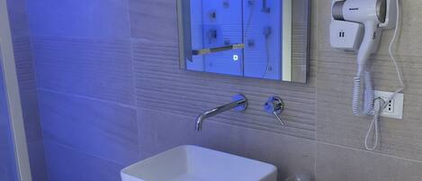 A modern bathroom with a white sink, a mirror above it, and a hairdryer mounted on the wall.