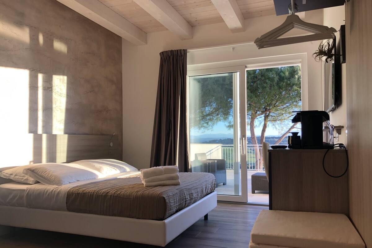 Un dormitorio con cama, una mesita de noche con cafetera y vistas al exterior a través de un ventanal corredero.