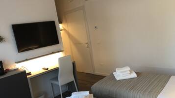 Habitación de hotel con cama, escritorio con silla, televisor en la pared y puerta que da a otra habitación.