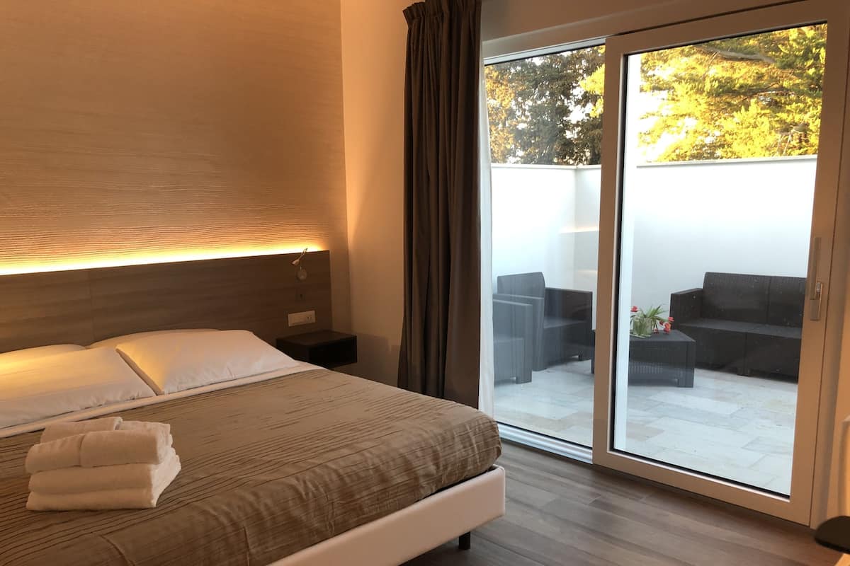 Un dormitorio con cama, mesita de noche y vista a un área de estar exterior a través de un ventanal.