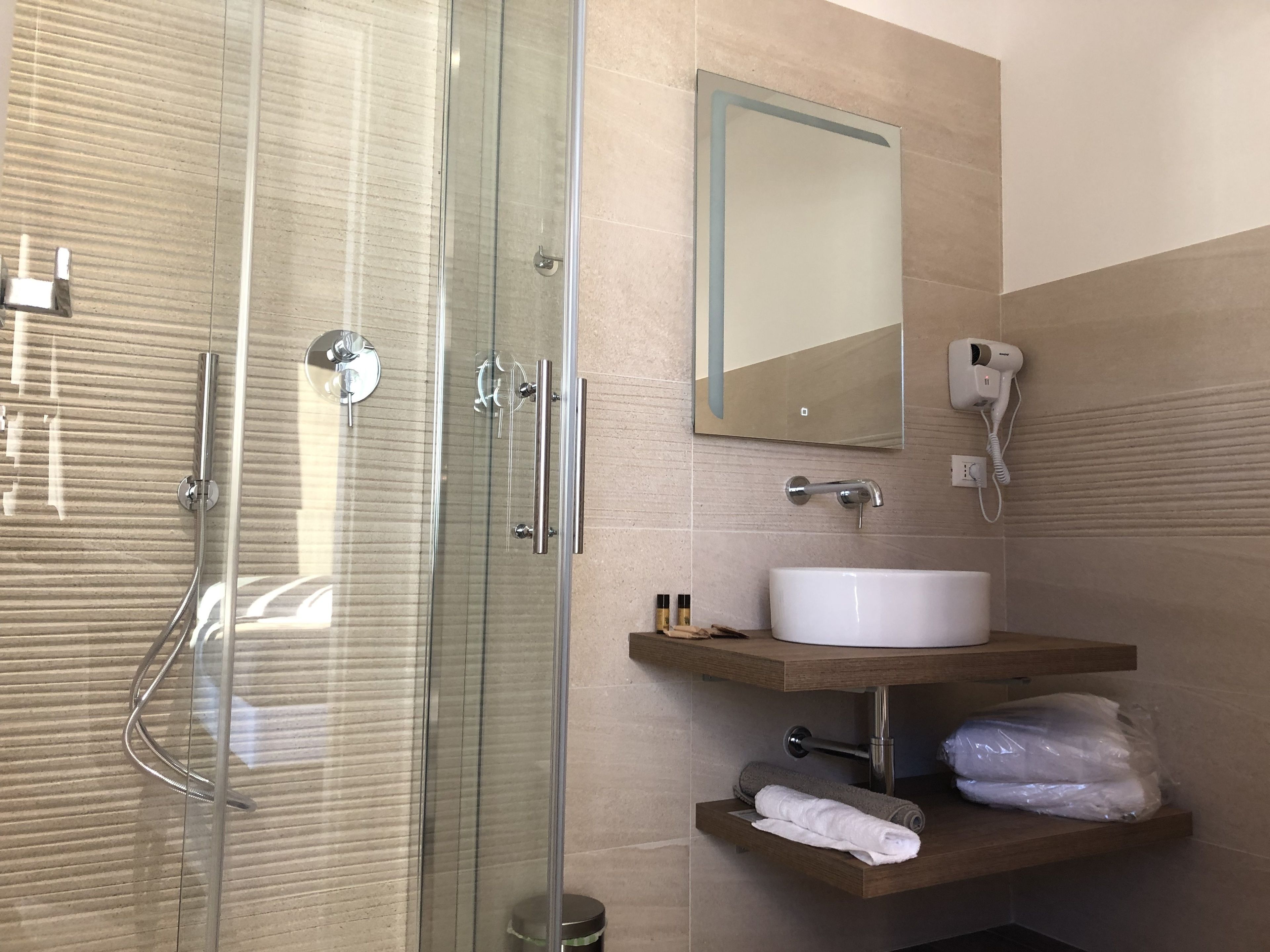 A modern bathroom with a glass shower enclosure, a white sink, a mirror, and a hairdryer on the wall.