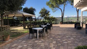 An outdoor patio with brick flooring, tables, chairs, and a pergola.
