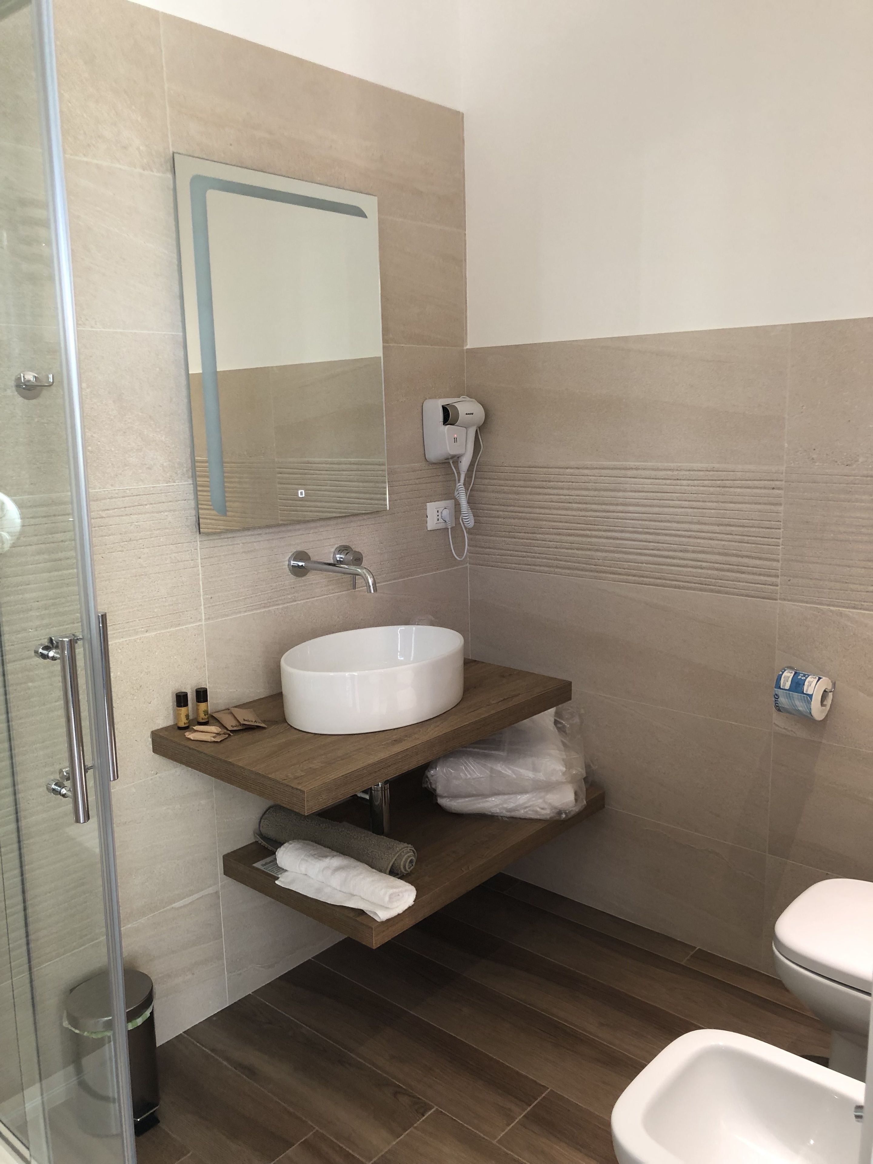 Une salle de bain moderne avec une douche à parois de verre, un lavabo blanc, un miroir, un sèche-cheveux et des toilettes.