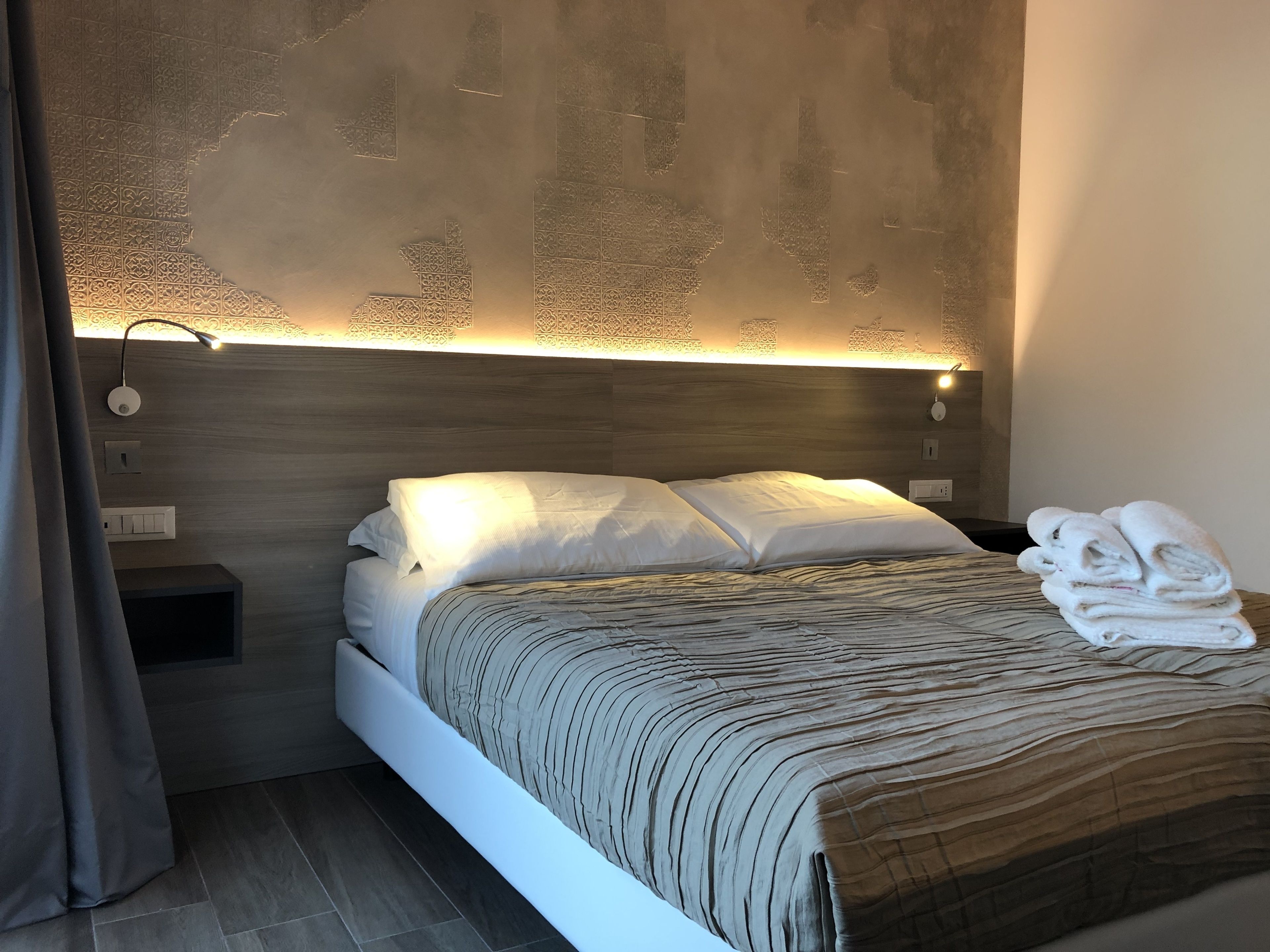 Un dormitorio moderno con cabecera de madera, una mesita de noche con lámpara y una cama bien tendida con manta a rayas.