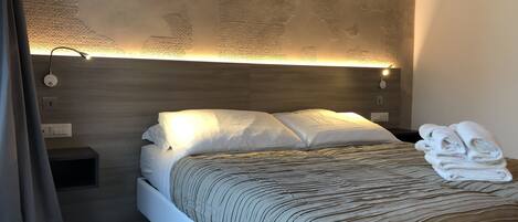 Un dormitorio moderno con cabecera de madera, una mesita de noche con lámpara y una cama bien tendida con manta a rayas.