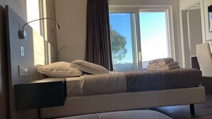 Un dormitorio moderno con cama, mesita de noche, lámpara y vistas al exterior.