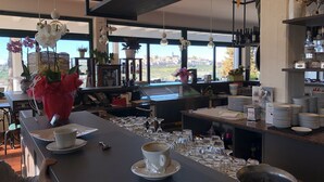 Un área de bar moderna con vistas a un paisaje urbano, que incluye una barra con vasos y una taza de café, un florero con orquídeas rojas y una variedad de botellas y vasos en estantes.