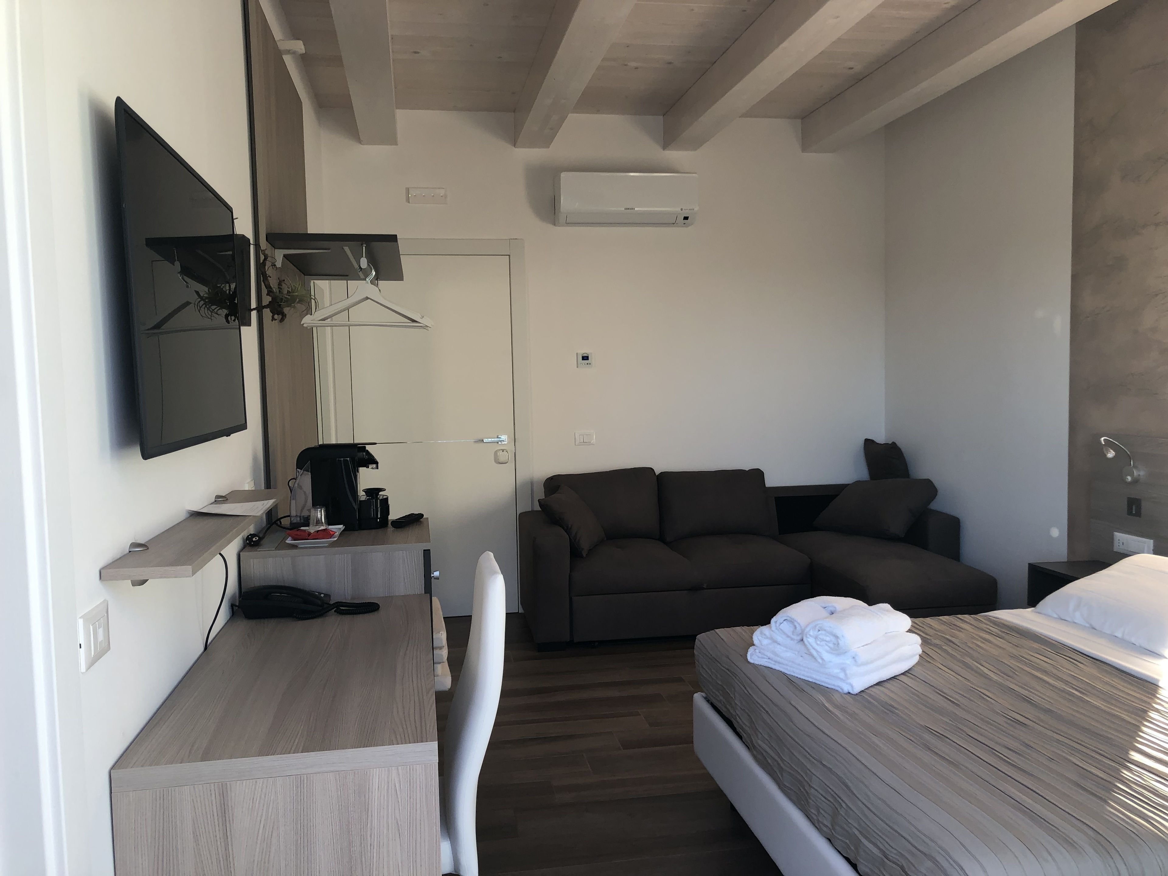 Une chambre d’hôtel moderne équipée d’un lit, d’un canapé, d’un bureau avec une machine à café, d’une télévision et d’un appareil de climatisation.