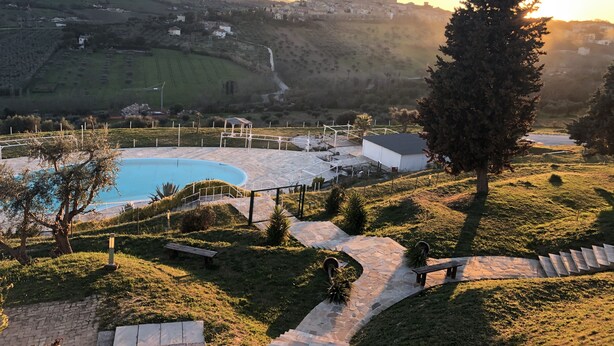 Zona de piscina con un sendero de piedra, bancos y vistas a un pueblo al fondo.