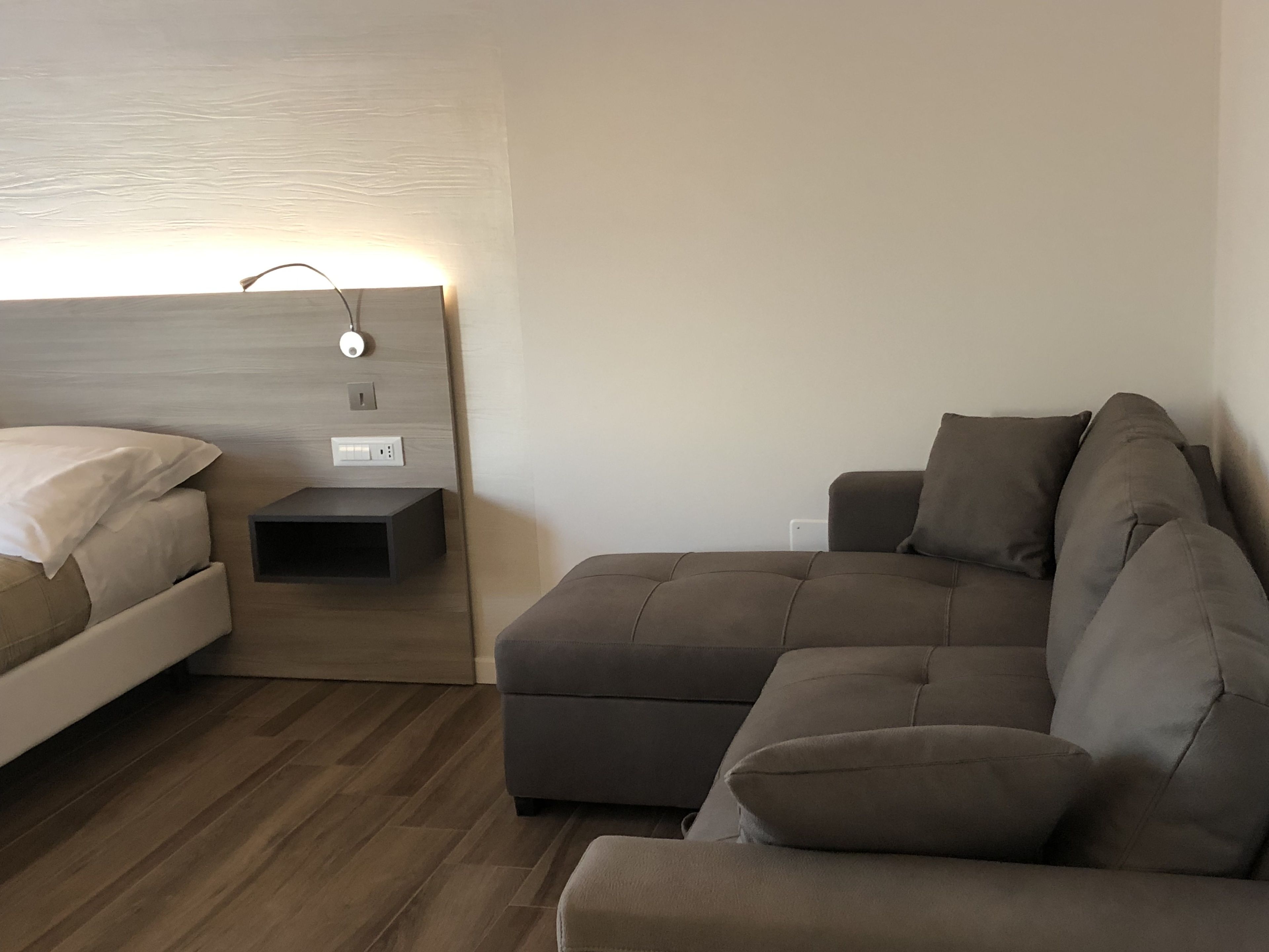 A modern bedroom with a bed, a nightstand, and a sofa.