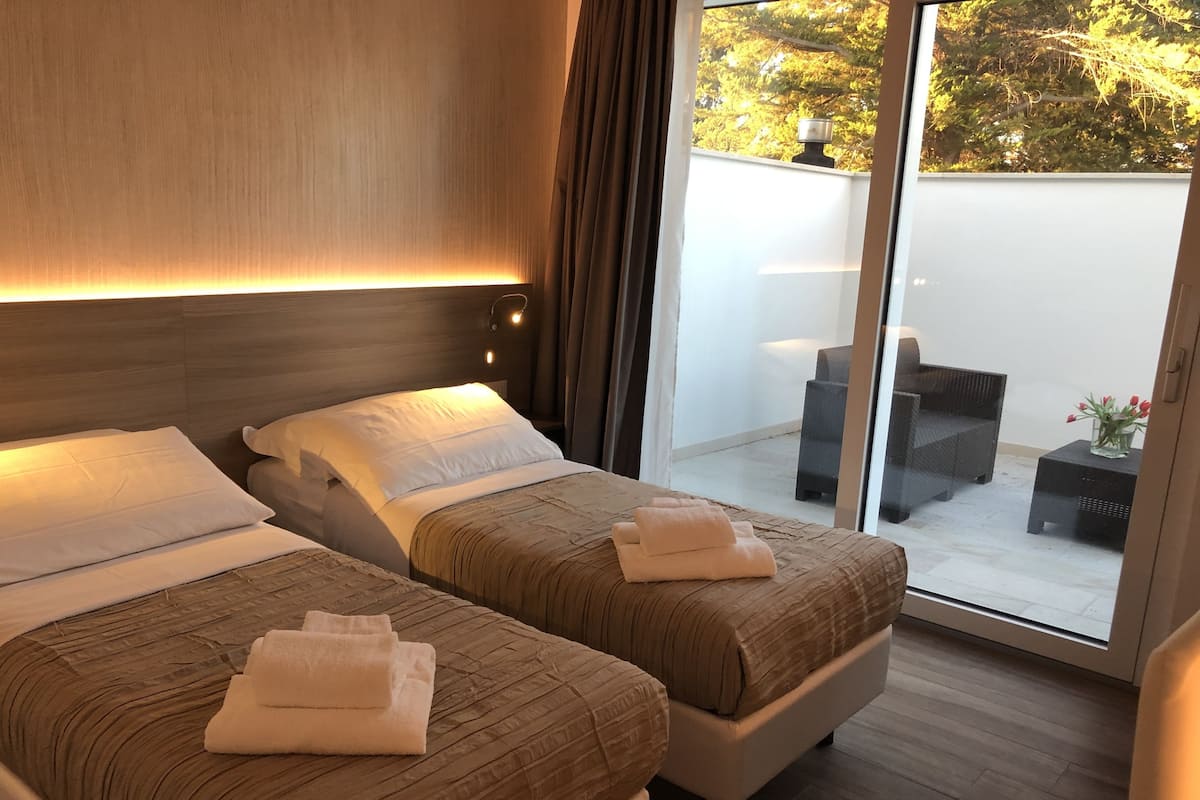 Habitación de hotel con dos camas y una puerta corrediza de vidrio que da a un área de estar al aire libre.