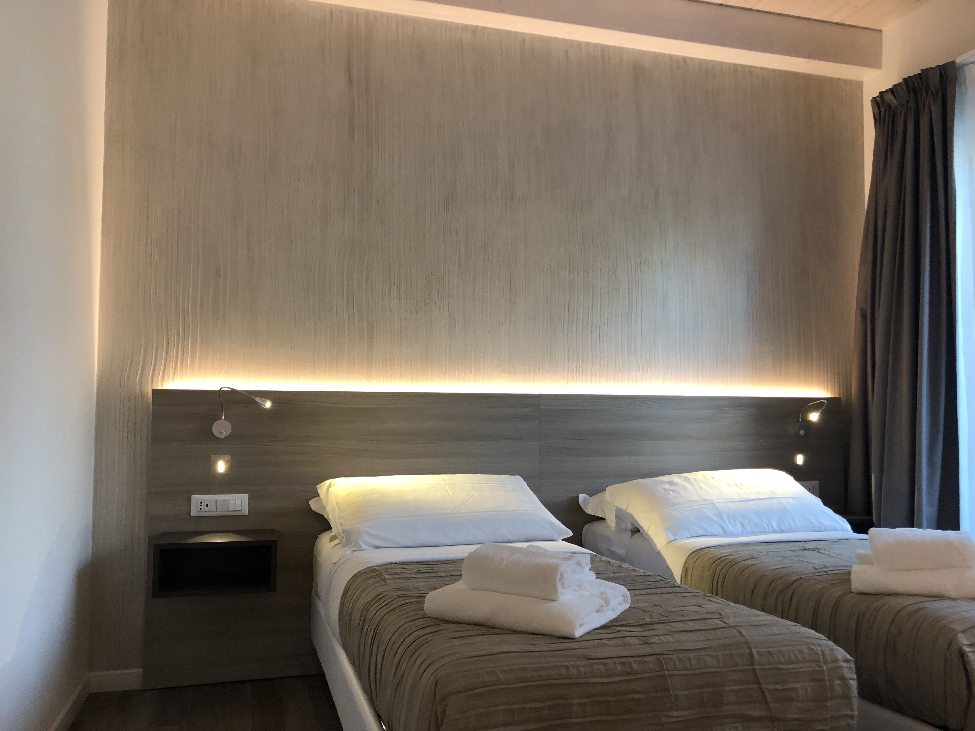 A hotel room with two beds, each with a headboard, bedside tables, and a wall-mounted light fixture.