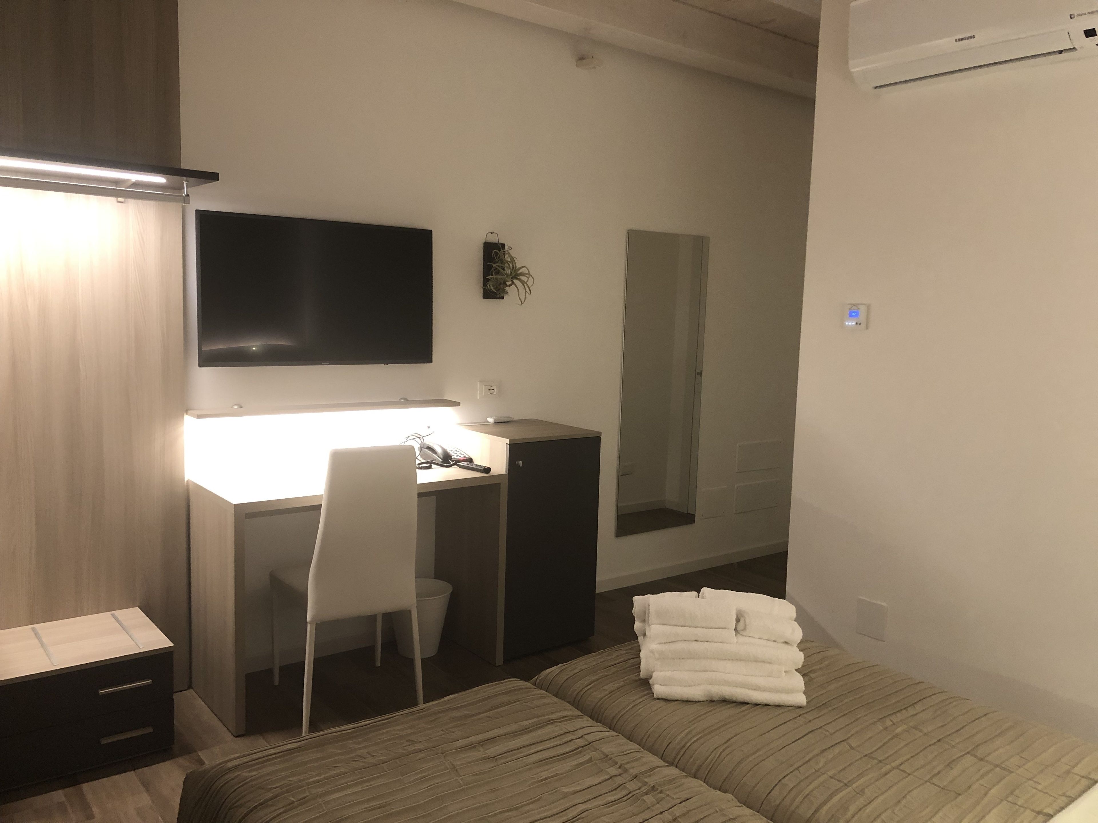 Ein Hotelzimmer mit einem Bett, einem Schreibtisch mit Stuhl, einem Flachbildfernseher, einem Spiegel und einem Stapel Handtücher.
