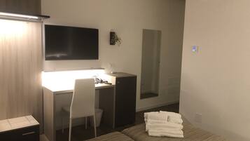 Ein Hotelzimmer mit einem Bett, einem Schreibtisch mit Stuhl, einem Flachbildfernseher, einem Spiegel und einem Stapel Handtücher.
