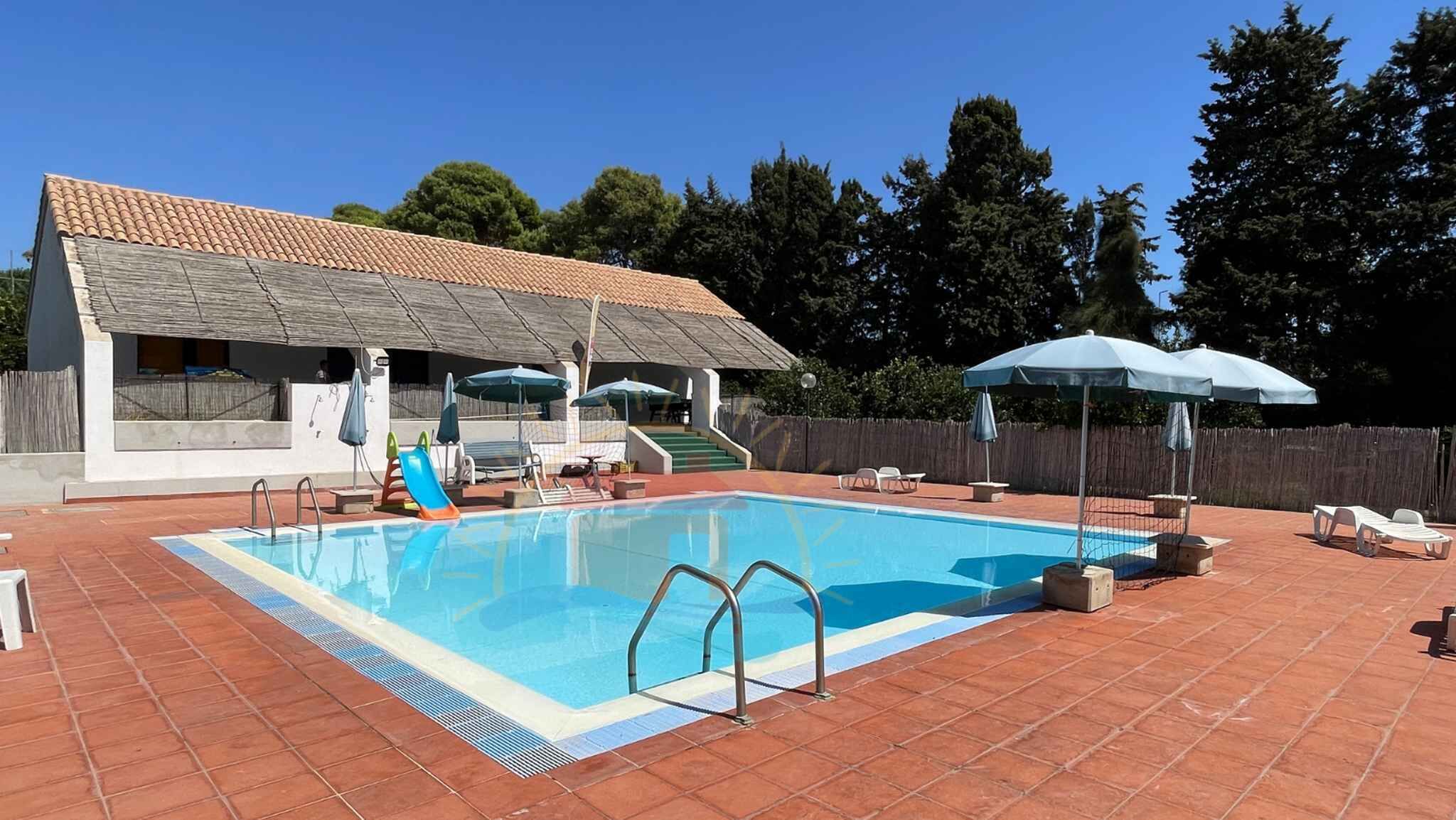 A swimming pool with a tiled deck, a slide, and umbrellas.