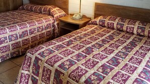 Habitación de hotel con dos camas, cabecero de madera, mesita de noche con lámpara y dos cuadros colgados en la pared.