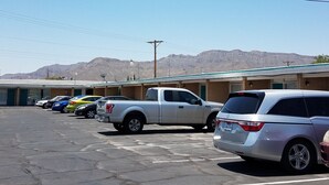 Un estacionamiento con varios autos, un edificio con múltiples entradas y montañas al fondo.