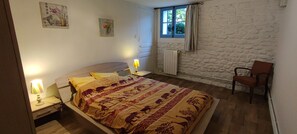 A bedroom with a bed, a chair, a nightstand, a lamp, and a window.