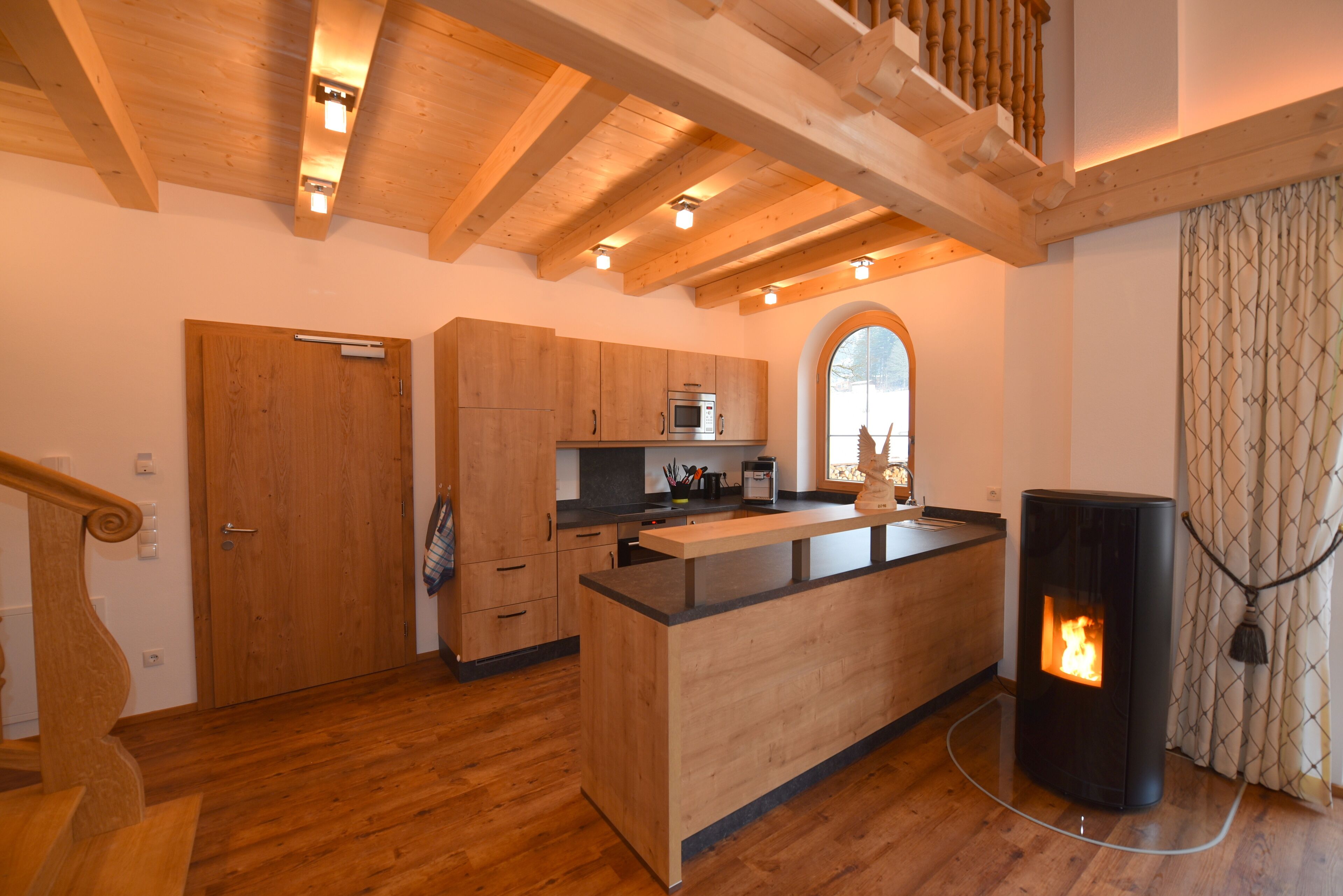 A modern kitchen with wooden cabinets, a central island, and a wood-burning stove.