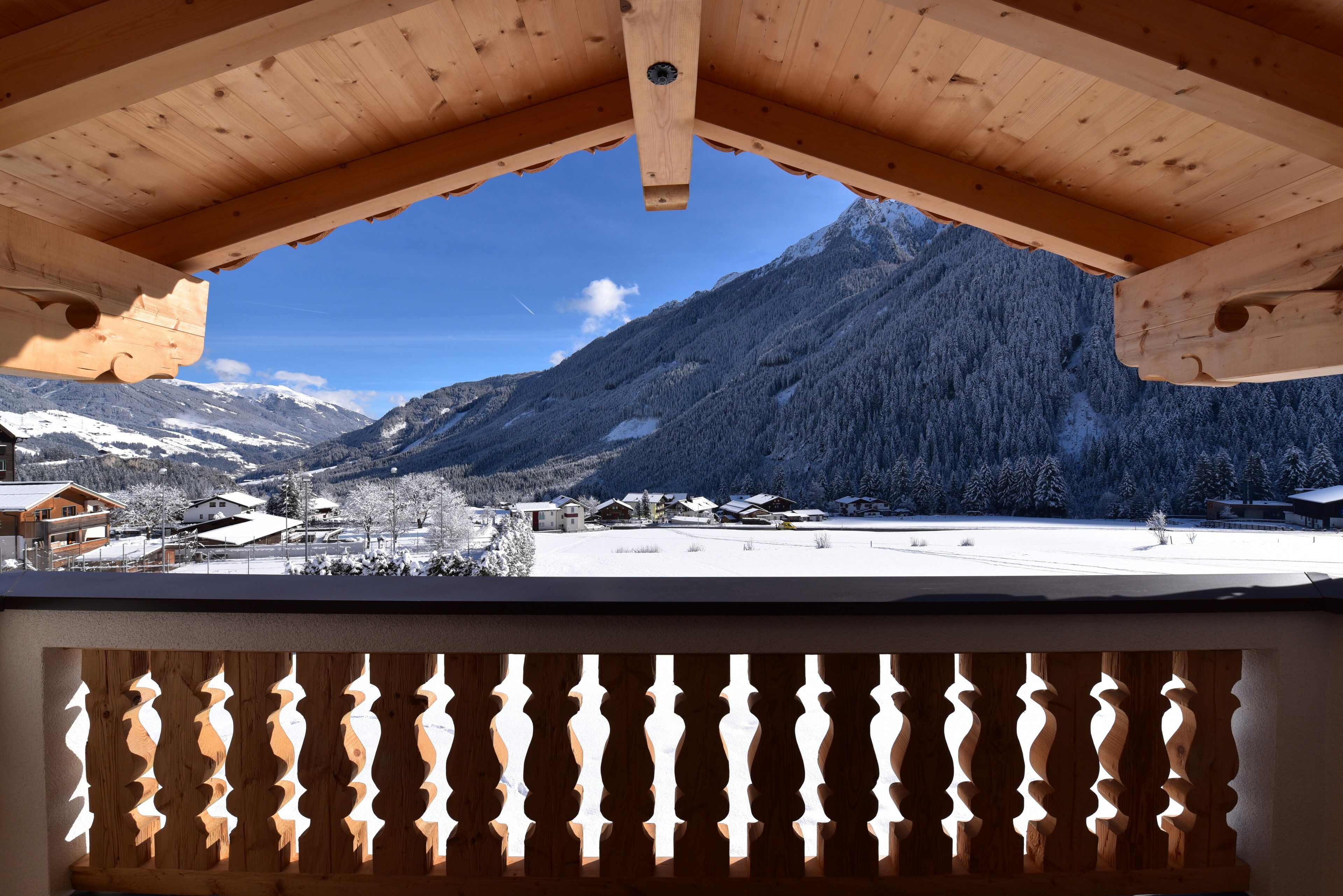 A wooden balcony with a view of snow-covered mountains and houses.