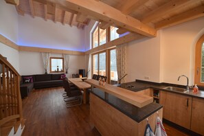 Une cuisine moderne avec un îlot central en bois, un coin repas avec un canapé et un escalier menant à un niveau supérieur.