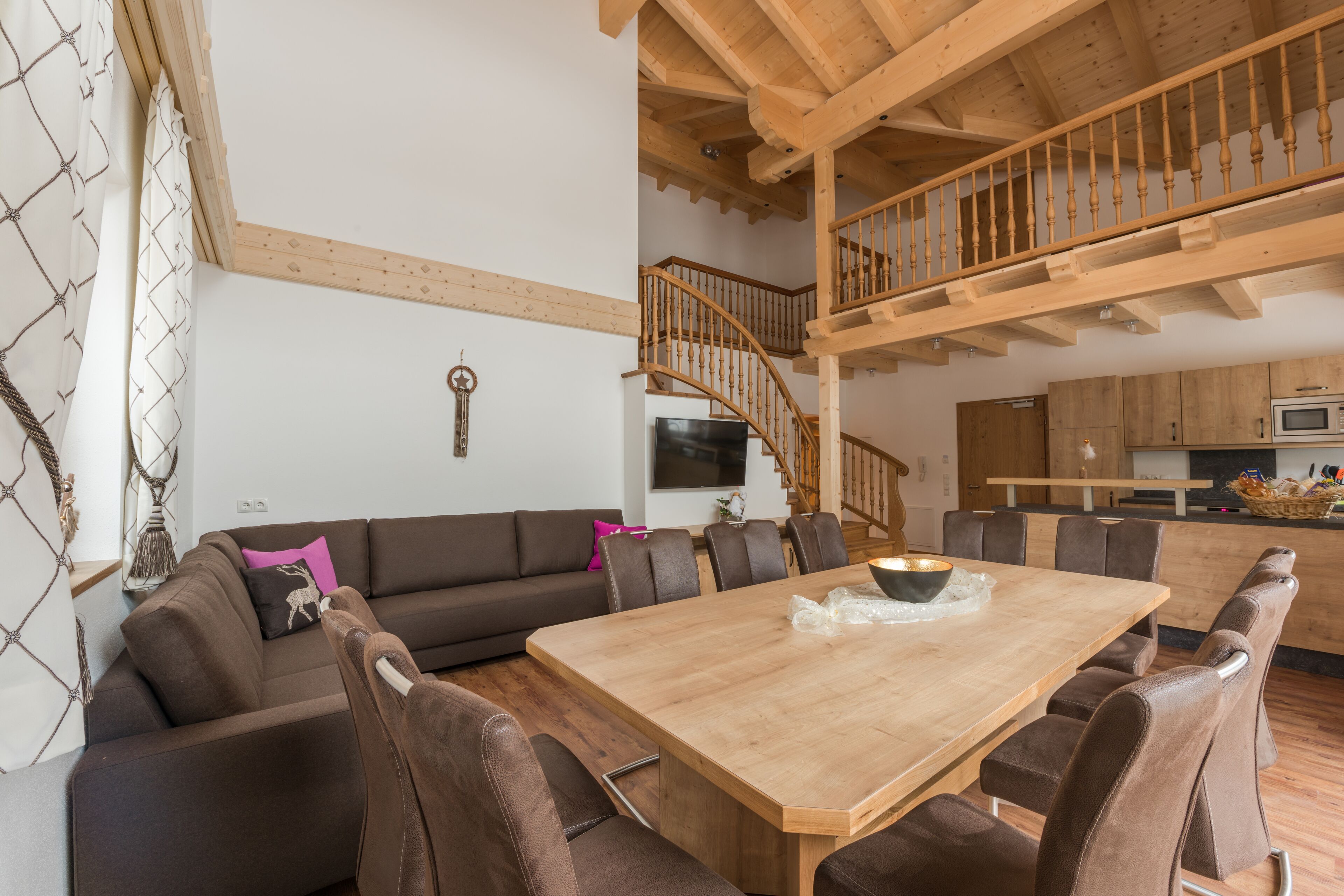 Un vaste espace de vie comprenant une table à manger en bois, des canapés en cuir marron et un escalier menant à un niveau supérieur.