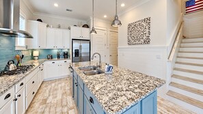 A kitchen with white cabinets, a granite countertop, stainless steel appliances, and a wooden staircase. - Holiday House - 3BR/2.5BA Prominence Home - Sleeps 8 - 6-Seat Golf Cart (Santa Rosa Beach)