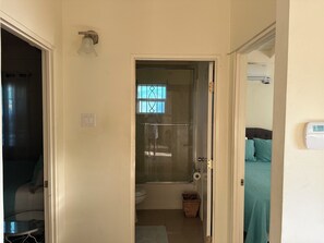 Ein schmaler Flur führt zu einem Badezimmer mit Dusche, Toilette und einer kleinen Mülltonne.