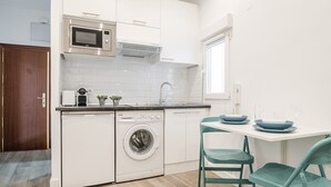 Une cuisine compacte équipée d’un four à micro-ondes, d’un four et d’un lave-linge. Elle comprend un évier, une fenêtre et une table avec des chaises.