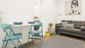 Un salon moderne avec un canapé gris, des fauteuils turquoise, une table blanche ornée d’une vaisselle bleue et un tapis noir et blanc à motifs.