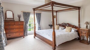 Un lit à baldaquin avec une structure en bois et un ciel de lit, une commode avec de nombreux tiroirs, un miroir et une table de chevet avec une lampe.