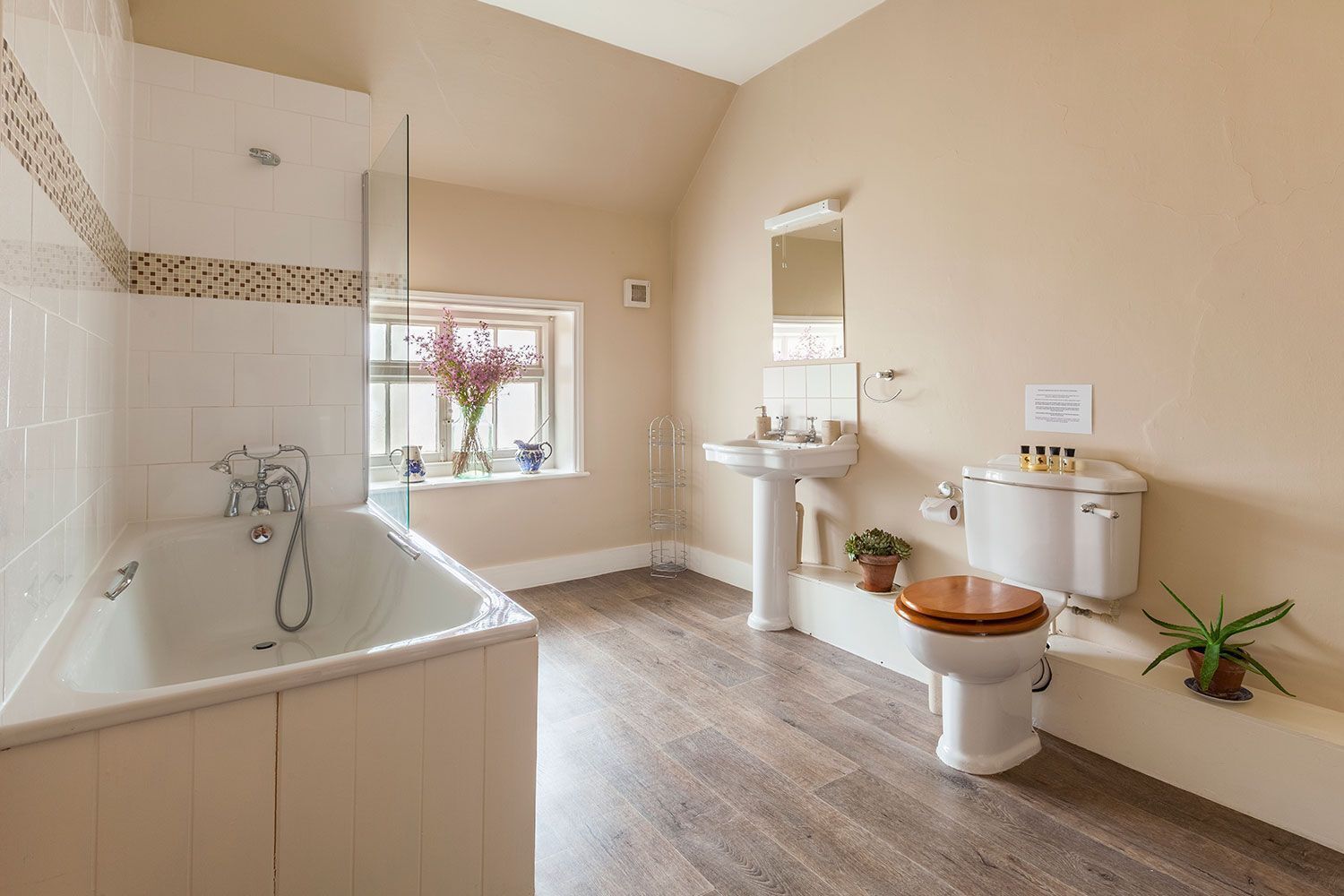 Un baño con bañera, lavamanos, inodoro y ventana con flores.