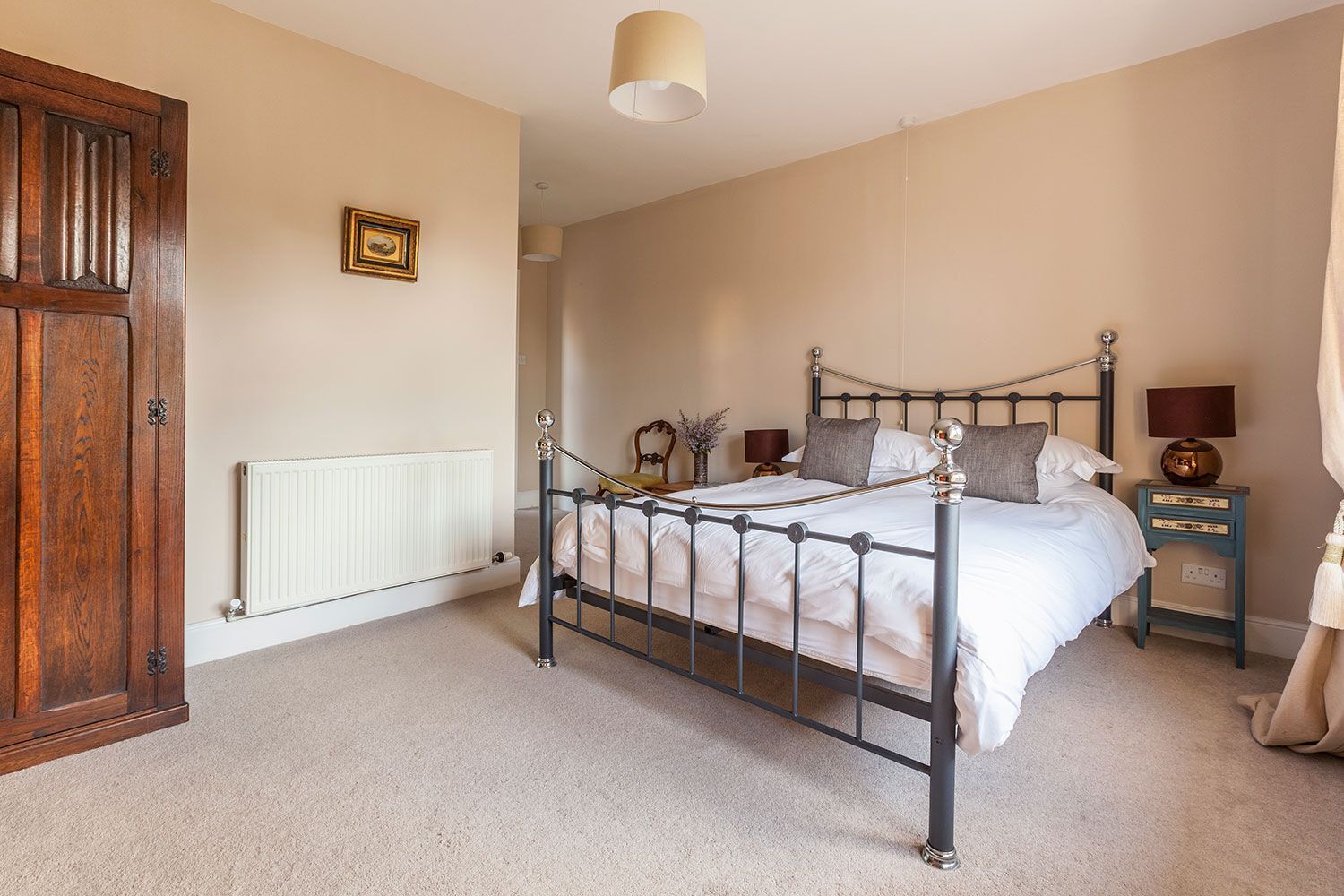 A bedroom with a four-poster bed, a wooden wardrobe, a bedside table with a lamp, and a radiator.