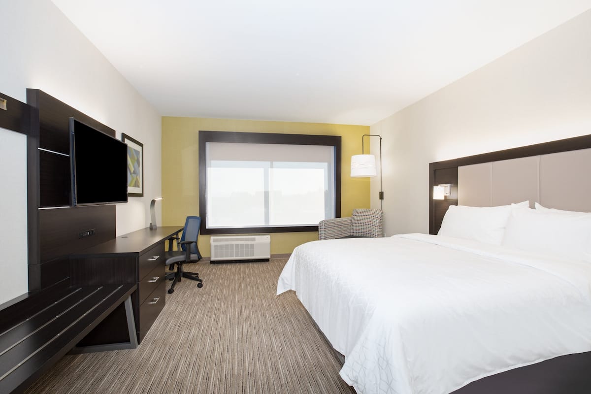 A hotel room with a large bed, a desk with a chair, a television, and a window with blinds.