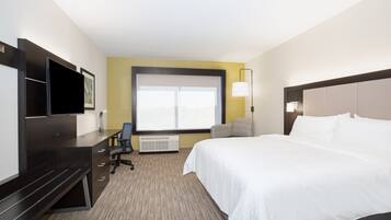 A hotel room with a large bed, a desk with a chair, a television, and a window with blinds.