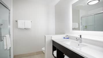 Une salle de bain moderne avec une douche à l’italienne en verre, un lavabo blanc avec un meuble-vasque foncé et un grand miroir au-dessus du lavabo.