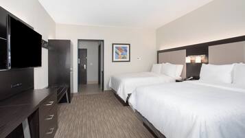 A hotel room with a flat-screen TV, two beds, a desk, and a framed picture on the wall.
