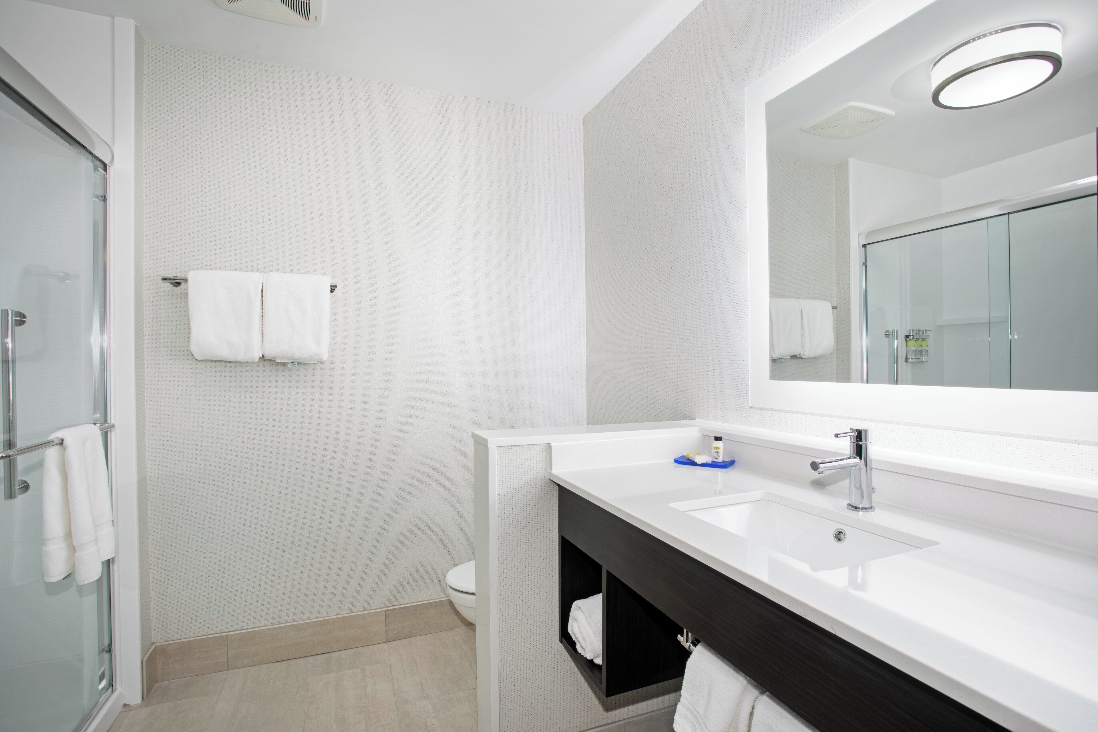 A modern bathroom with a glass shower enclosure, a white sink with a large mirror, and a dark vanity.