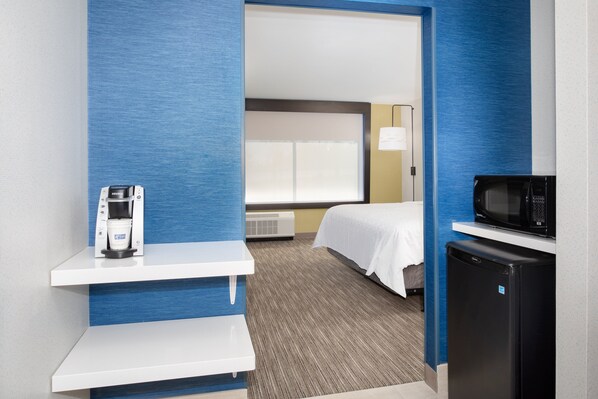 A hotel room with a bed, a microwave, a refrigerator, a coffee maker, and a small table.