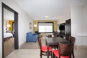 A hotel room with a dining area, a sofa, a TV, and a large window.