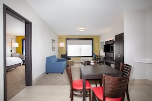Habitación de hotel con zona de comedor, sofá, televisor y ventana grande.