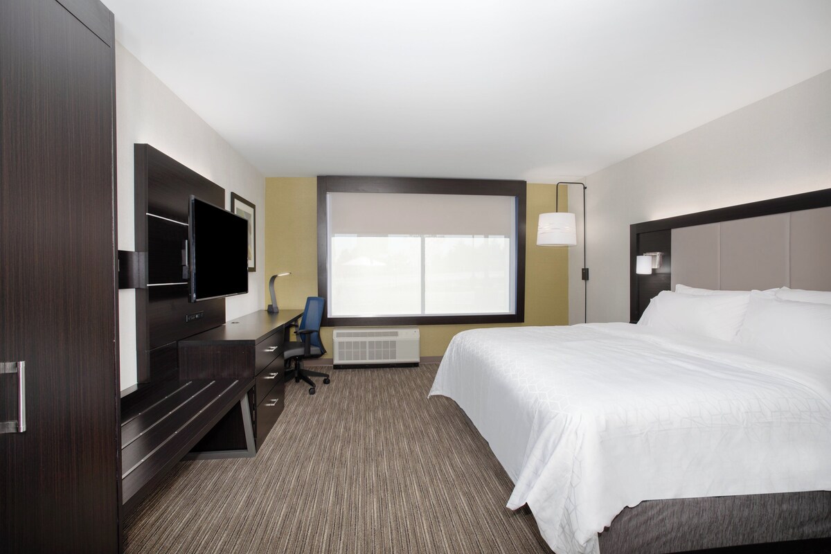 A hotel room with a bed, a desk with a chair, a television, and a window.