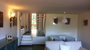 A living room with a sofa, a dining table, and a staircase leading to an outdoor area.