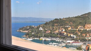 A coastal town with buildings on a hillside, a marina with boats, and a clear view of the sea.