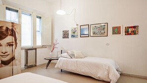 A bedroom with a bed, a bedside table, a lamp, and a window.