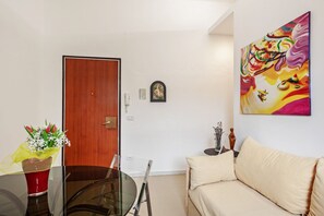 A room with a wooden door, a glass table with a red vase, a beige sofa, and a colorful painting on the wall. - GuestHost - NEW!Palazzo dei Diamanti! Pets Friendly (Ferrara)